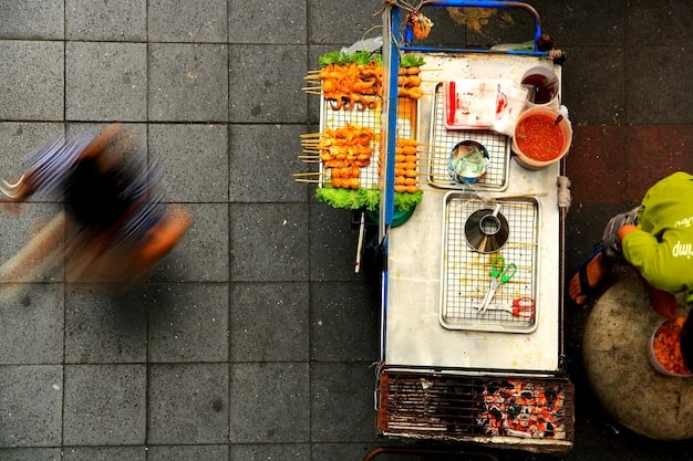 A top-down shot of a street food vendor's cart, showcasing a variety of colorful tteokbokki dishes, with customers lining up and the vendor preparing the food.